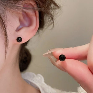Close-up of minimalist black spherical stud earrings with high-gloss finish on model