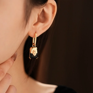 Close-up of golden lion head relief on black rectangular stone drop earrings