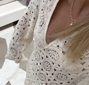 Detail of white crochet lace dress featuring intricate V-neck and floral hollow embroidery