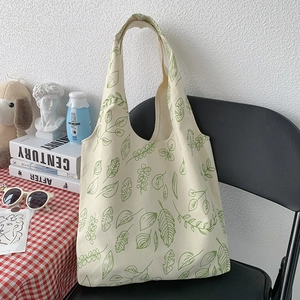 Detail of canvas tote bag featuring green leaf print hanging on a black chair