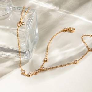 Gold stainless steel finger bracelet with round zircons draped on a glass perfume bottle