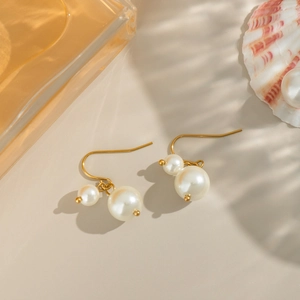 Gros plan d'élégantes boucles d'oreilles dorées avec doubles perles blanches sur fond chaud