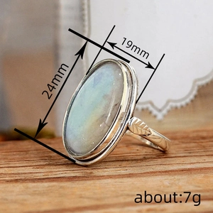Vintage oval moonstone ring with leaf-engraved silver band on a wooden base