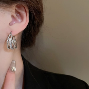 Macro close-up of a silver multi-layer zircon hoop earring worn by a model in warm light