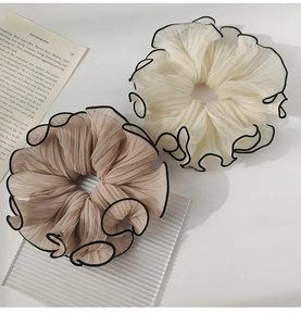 Close-up of pleated beige chiffon scrunchies with black piping on white tabletop