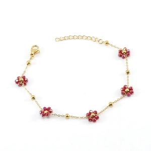 Detail of gold chain bracelet featuring red faceted bead flowers and lobster clasp