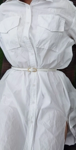 Close-up of a slim white leather belt with a gold metal buckle on a white shirt dress