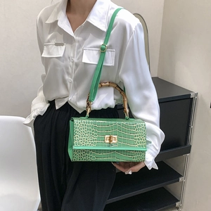 Close-up of green crocodile embossed bag with natural bamboo handle and twist lock detail