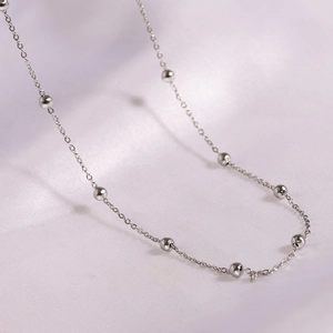 Macro shot of minimalist stainless steel O-chain necklace with beads on white silk