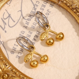 Détail de boucles d'oreilles cerises bicolores or et argent sur papier vintage