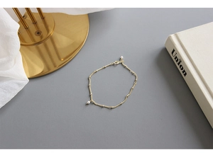 Close-up of minimalist gold beaded chain bracelet featuring a delicate pearl pendant detail