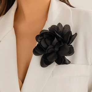 Detailed macro view of a black fabric rose brooch pinned on a white formal suit jacket