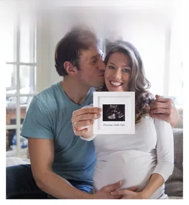 Detail of white square sonogram photo frame with Precious Little One text held by a couple