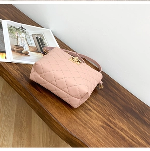 Detailed shot of pink quilted crossbody bucket bag with gold metal clasp on wooden bench