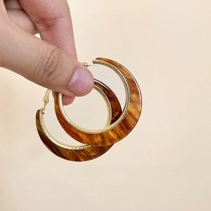 Bohemian acrylic amber round hoop earrings with golden metal trim held in hand