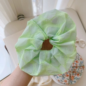 Close-up of a large light green floral scrunchie with sheer fabric and pleated texture