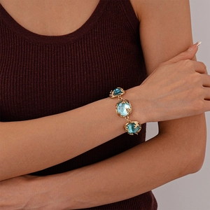Detailed macro view of gold chain bracelet with blue resin stones and leaf carvings