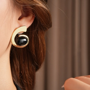 Gros plan de boucles d'oreilles dorées géométriques avec perle noire sur un mannequin