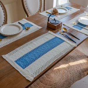 Blue and white woven cotton placemats with fringe details on dark wooden dining table
