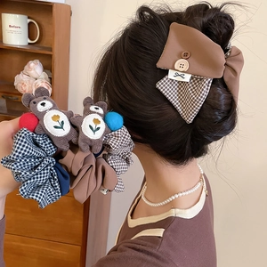 Detail of plaid bow hair clip and plush bear scrunchie set in warm brown tones