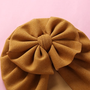 Macro shot of ginger yellow knit baby turban hat featuring a large 3D bow decoration