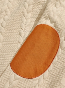 Close-up of oatmeal cable knit fabric with a contrasting orange oval patch detail