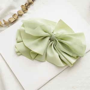 Close-up of light green fabric bow hair clip with ribbons on elegant white background