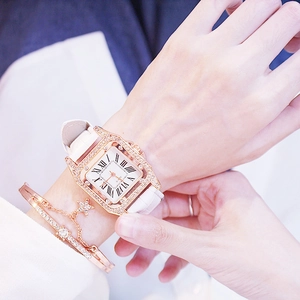 Detail view of square rose gold watch with crystals and white leather strap on wrist