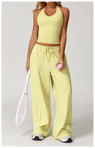 Woman in pale yellow yoga tank top and wide-leg pants holding a tennis racket