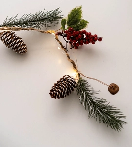 Close-up of warm LED Christmas string lights with pine cones, red berries, and copper bells