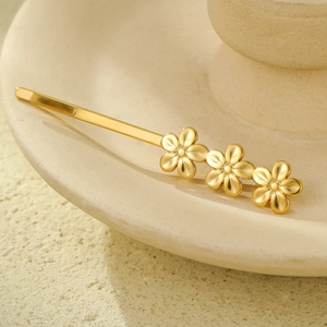 Macro shot of gold floral hair clip with pearl accents on a ceramic plate background