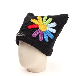 Detail of a black cat ear beanie featuring a colorful crochet daisy and silver safety pin