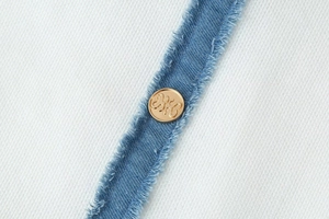 Détail du tissu en maille blanche avec bordure en denim et bouton en métal doré