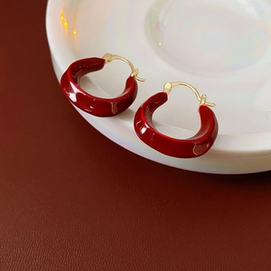 Macro detail of dark red enamel C-shape hoop earrings on white ceramic dish