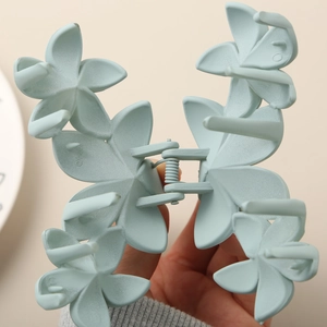 Detail of matte light blue floral claw clip showing 3D petals and metal spring mechanism