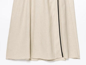 Detailaufnahme des beigen Leinenkleid-Saums mit markanter schwarzer vertikaler Kontrastborte
