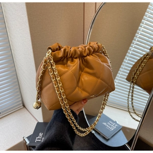 Detail of a brown quilted cloud bag with a chunky gold chain strap in a cozy interior
