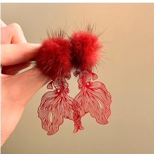 Macro shot of red pom-pom earrings featuring intricate metal hollow goldfish tail details