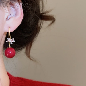 Close-up of gold-plated red resin bead earrings worn by a model in a red sweater