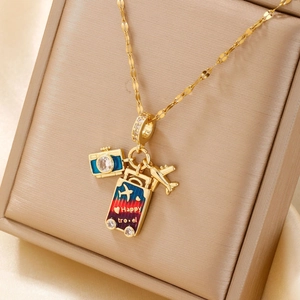 Golden travel themed necklace with camera suitcase and airplane pendants on velvet box