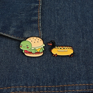 Détail des pin's émaillés tortue burger et teckel hot-dog sur tissu en denim