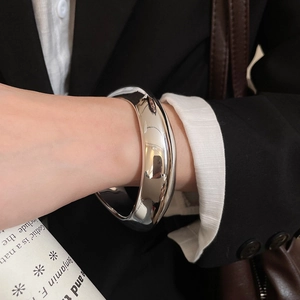 Detailed view of wide polished silver bangle with mirror finish on model wearing black blazer