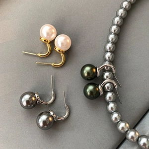 Close-up of pearl hook earrings in white, dark grey and green with metallic hooks