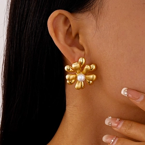 Gros plan d'une boucle d'oreille fleur en métal doré avec perle portée par un modèle