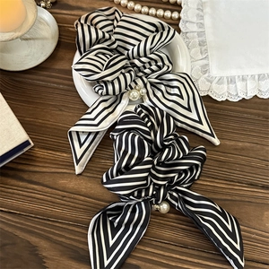 Close-up of silk-like striped bow scrunchies with elegant pearls on a vintage background