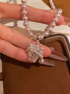 Detail of pink pearl necklace featuring a floral basket pendant in a jewelry box
