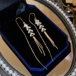 Detailed view of gold fishbone earrings with zircons and tassels in a velvet box