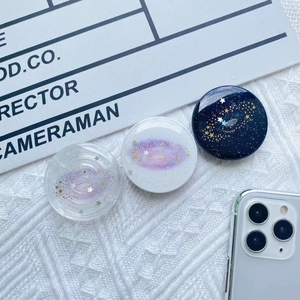 Close-up of three sparkling galaxy-themed telescopic phone grips with glitter finish