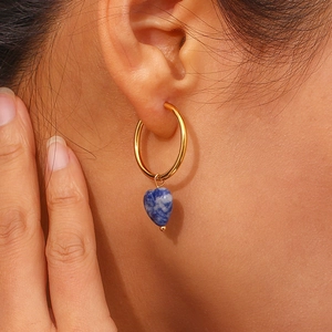 Close-up of golden hoop earring with heart-shaped blue natural stone on model
