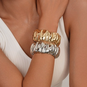 Detail of wide metal cuff bracelets with textured ripple design in gold and silver finish
